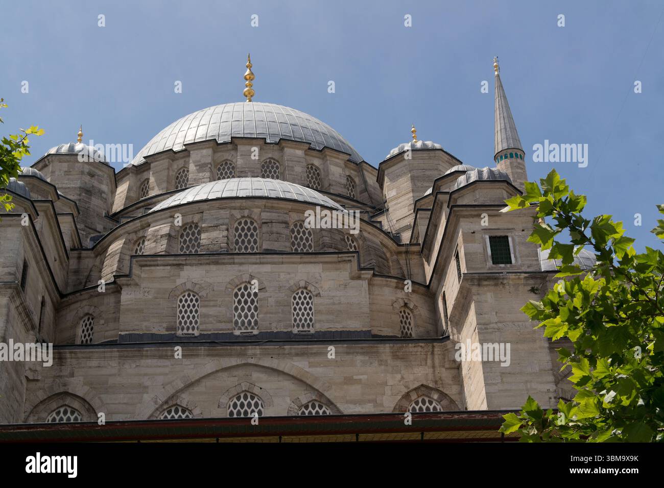 Besucher bewundern die komplizierte Architektur einer Moschee in Istanbul unter strahlend blauem Himmel, die das reiche kulturelle Erbe der Stadt widerspiegelt. Stockfoto