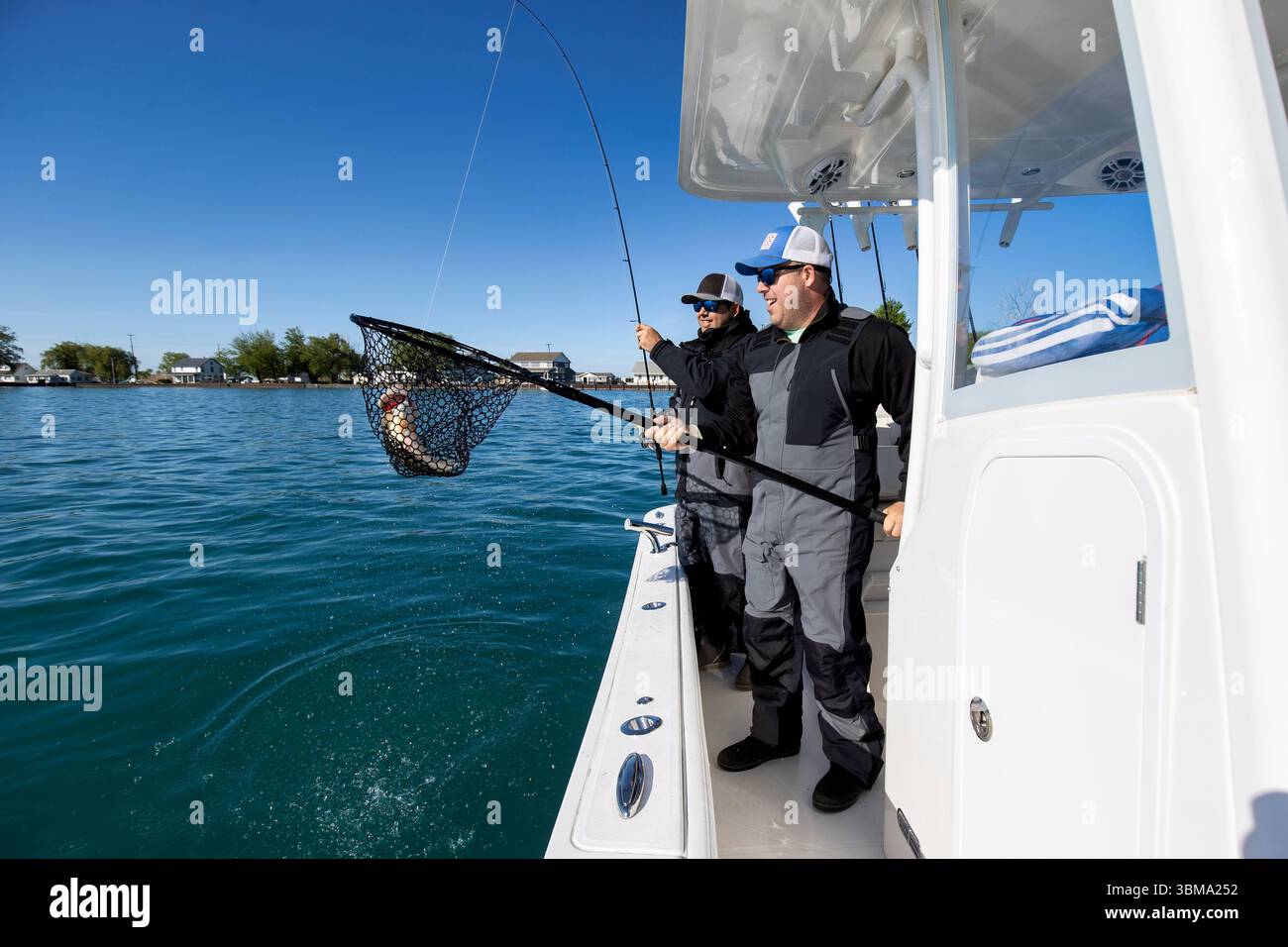 Zwei Männer auf einem Boot, einer hält ein Netz mit einem Fisch, den sie gefangen haben Stockfoto