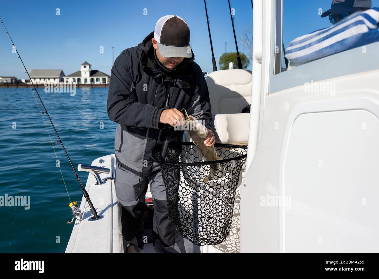 Mann auf einem Boot, der den Haken von einem Fisch entfernt, den er gefangen hat Stockfoto