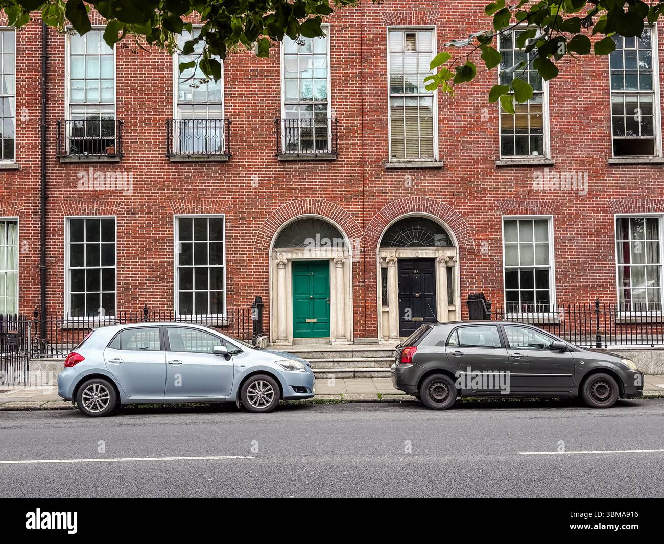 Autos parkten auf einer Straße in Dublin, Irland. Zwei Fließhecken parken vor einem traditionellen georgianischen Backsteingebäude mit bogenförmigen Eingängen. Stockfoto