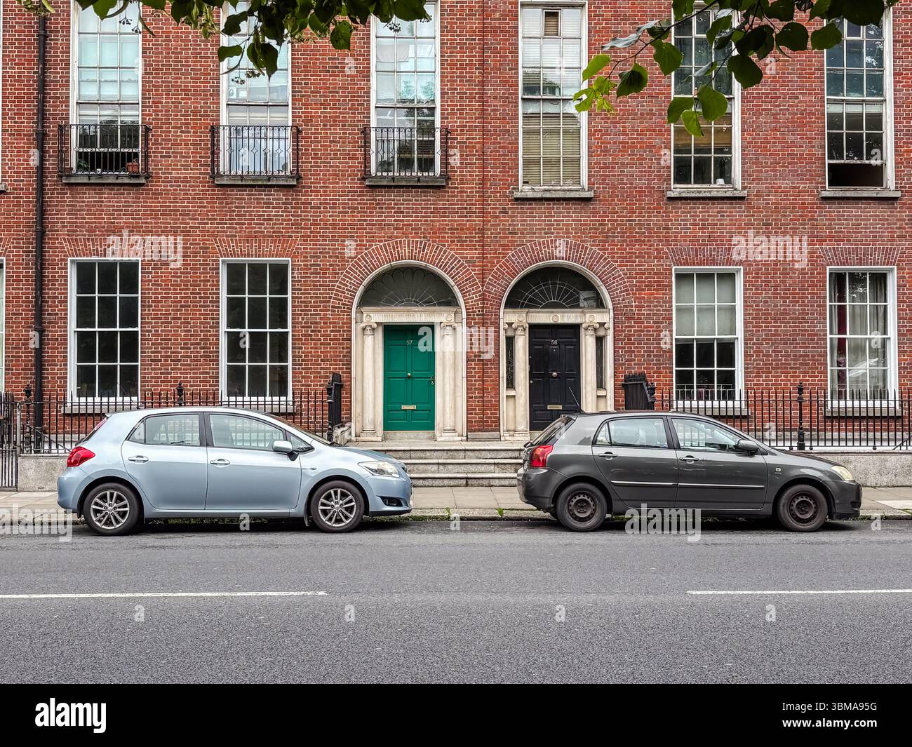 Autos parkten auf der Straße, Dublin. Zwei Autos parkten auf einer Stadtstraße vor klassischen Ziegelhäusern im georgianischen Stil. Stockfoto