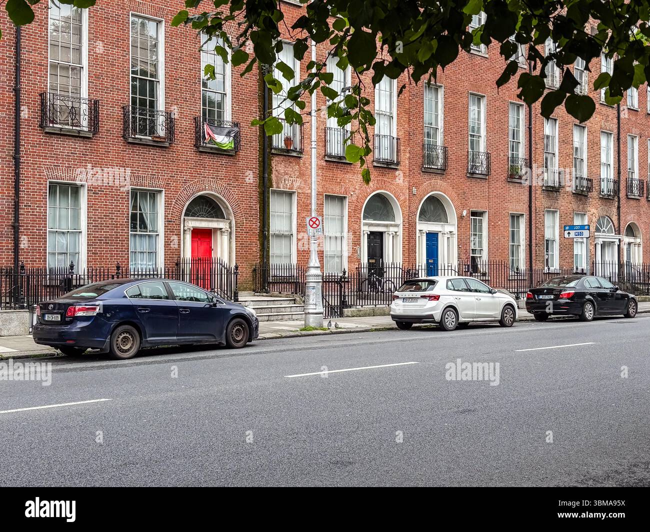 Autos parkten auf einer Straße in Dublin vor klassischen Ziegelsteingebäuden. Rote Türen verleihen der urbanen Szene Charakter. Stockfoto