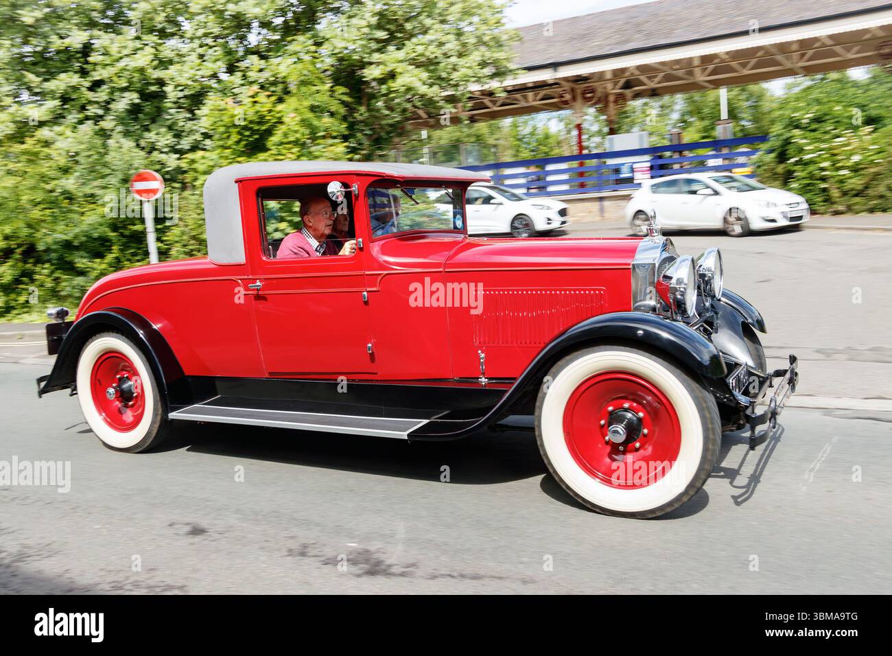 Ein roter Klassiker von Packard mit weißen Reifen, der mit einem Mann im Inneren eine Kappe trägt, die Straße hinunter fährt Stockfoto