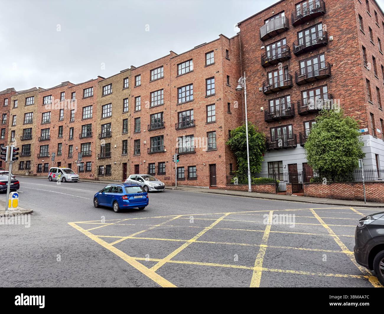 Apartment-Gebäude in einer Straßenszene der Stadt mit Autos an einem bewölkten Tag in Dublin, Irland. Modernes Backsteingebäude. Stockfoto