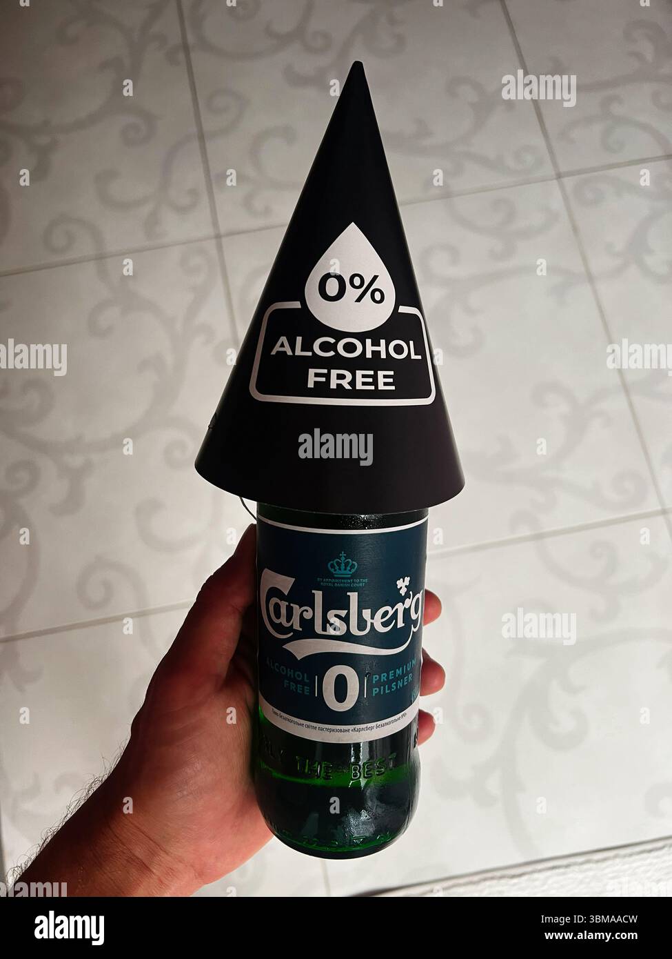 Kiew, Ukraine - 24. Juni 2025: Alkoholfreies Carlsberg-Biergetränk in der Hand mit Markenkappe, die oben auf gemustertem Boden steht. Stockfoto