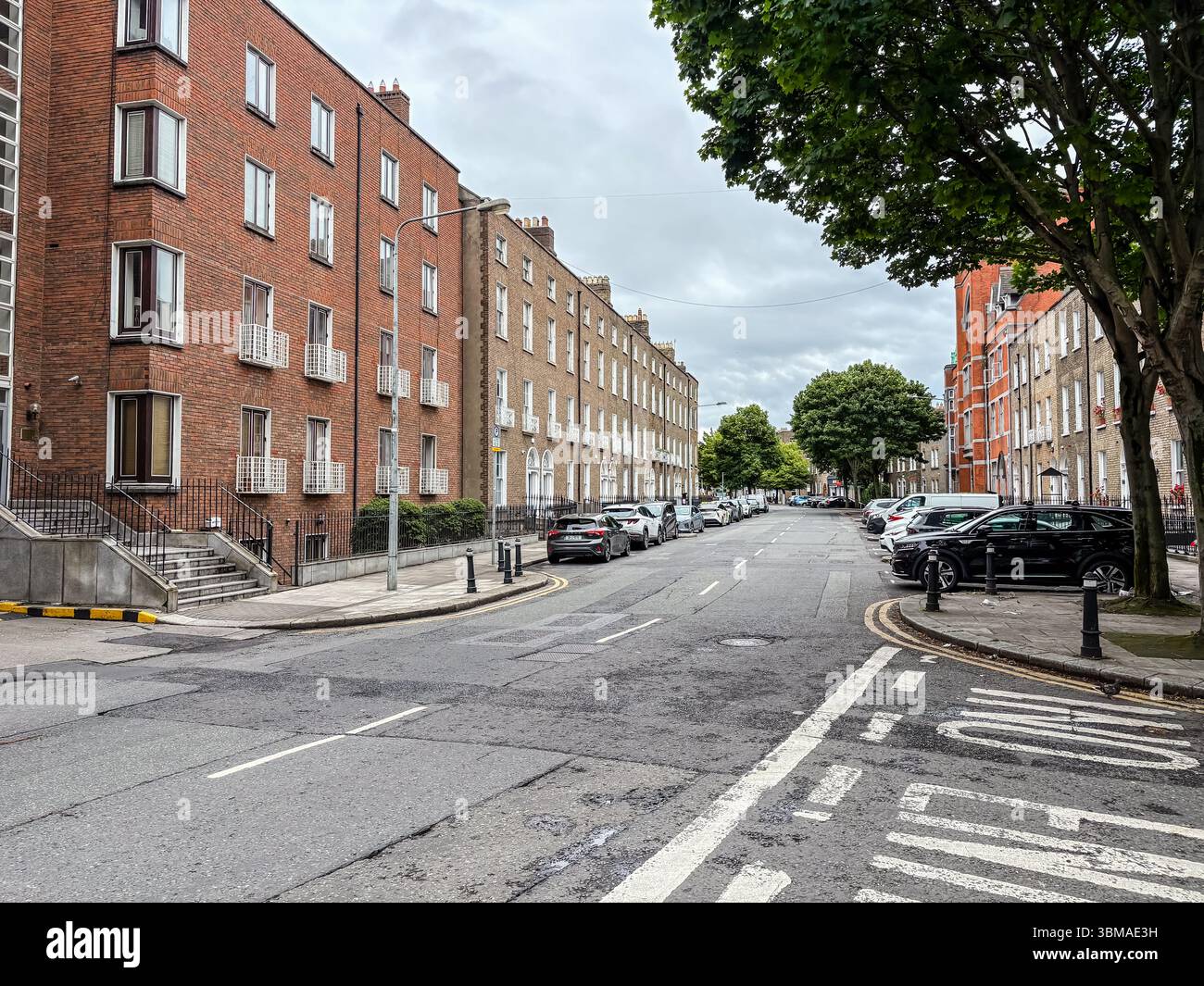 Die Baggot Street in Dublin, Irland, besticht durch elegante georgianische Architektur entlang einer historischen Stadtdurchgangsstraße mit parkenden Autos und alten Bäumen. Stockfoto