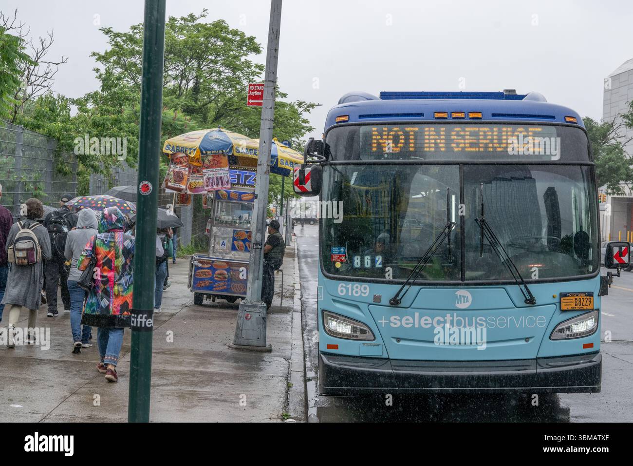 Ein New York City Bus mit nicht in Betrieb Schild im Regen mit New yorkern, die mit Schirmen vorbeilaufen Stockfoto