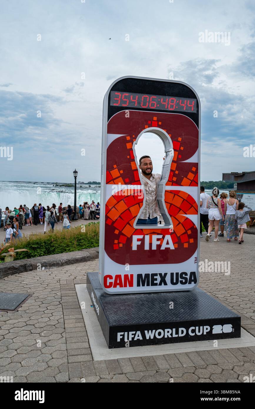 Ein lächelnder Tourist posiert vor einem FIFA-Werbefoto-Schild vor den Horseshoe Falls. Die FIFA 2026 findet in Kanada, Mexiko und den USA statt Stockfoto