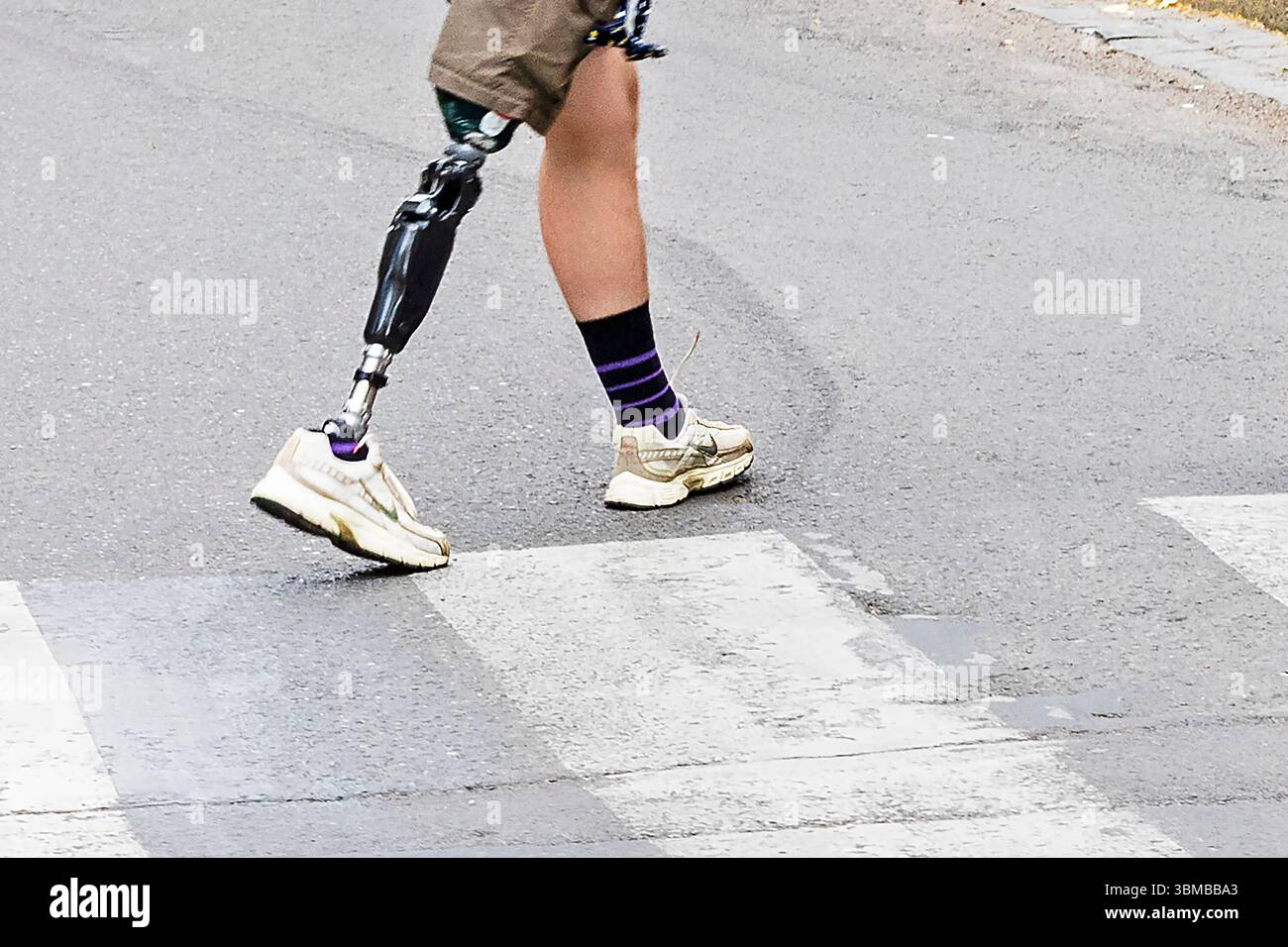 Ein junger Mann mit einer Beinprothese überquert die Straße in der Stadt Stockfoto