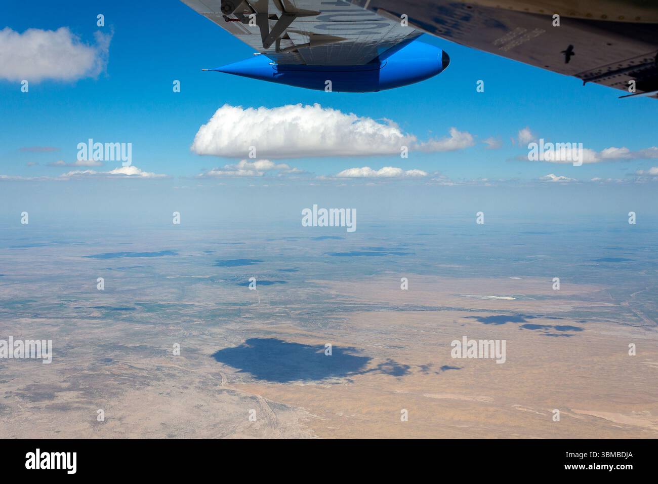 Die Luftperspektive fängt die Weite der usbekischen Wüste ein, eingerahmt von einem Flügel eines Flugzeugs, unter einem hellblauen Himmel mit flauschigen Wolken. Stockfoto