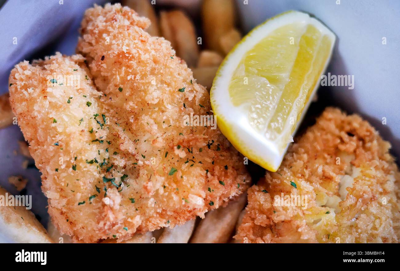 Klassisches traditionelles englisches oder britisches kulinarisches Delikatessen Fish and Chips, goldener, frittierter Fisch mit Zitronenscheiben in einer Papierkarton zum Mitnehmen als Mittagessen Stockfoto