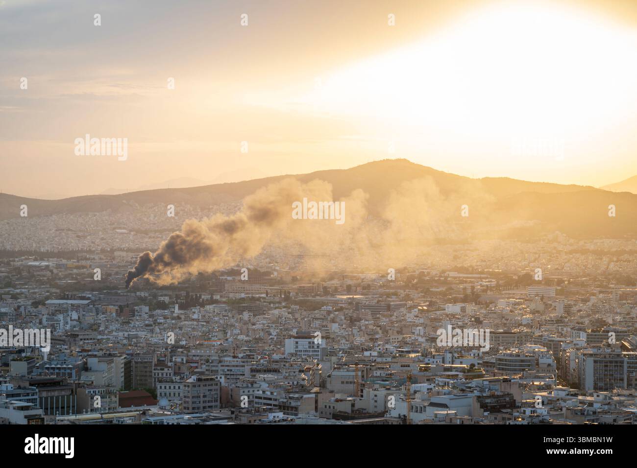 In den Vororten von Athen, Griechenland, brennt ein Feuer, das schwarzen Rauch in die Luft spuckt und den Sonnenuntergang in der Ferne zu verdecken droht Stockfoto