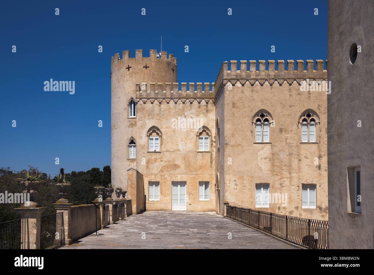Entdecken Sie die majestätische Architektur der Burg Donnafugata unter einem klaren blauen Himmel, die zu Erkundungen und Reflexionen in Sizilien, Italien, einlädt Stockfoto