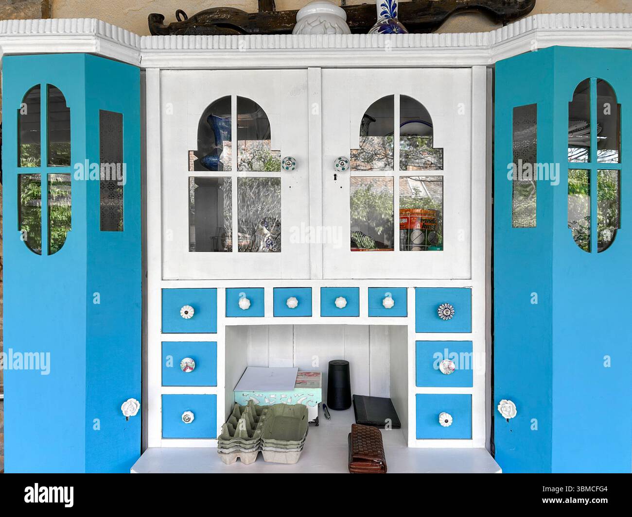 Charmanter Vintage-Küchenschrank in Blau und weiß mit dekorativen Knöpfen, Glasplatten und vielseitigen Schubladen, perfekt für rustikale oder Retro-insp - Smartphone-aufgenommenes Stockfoto