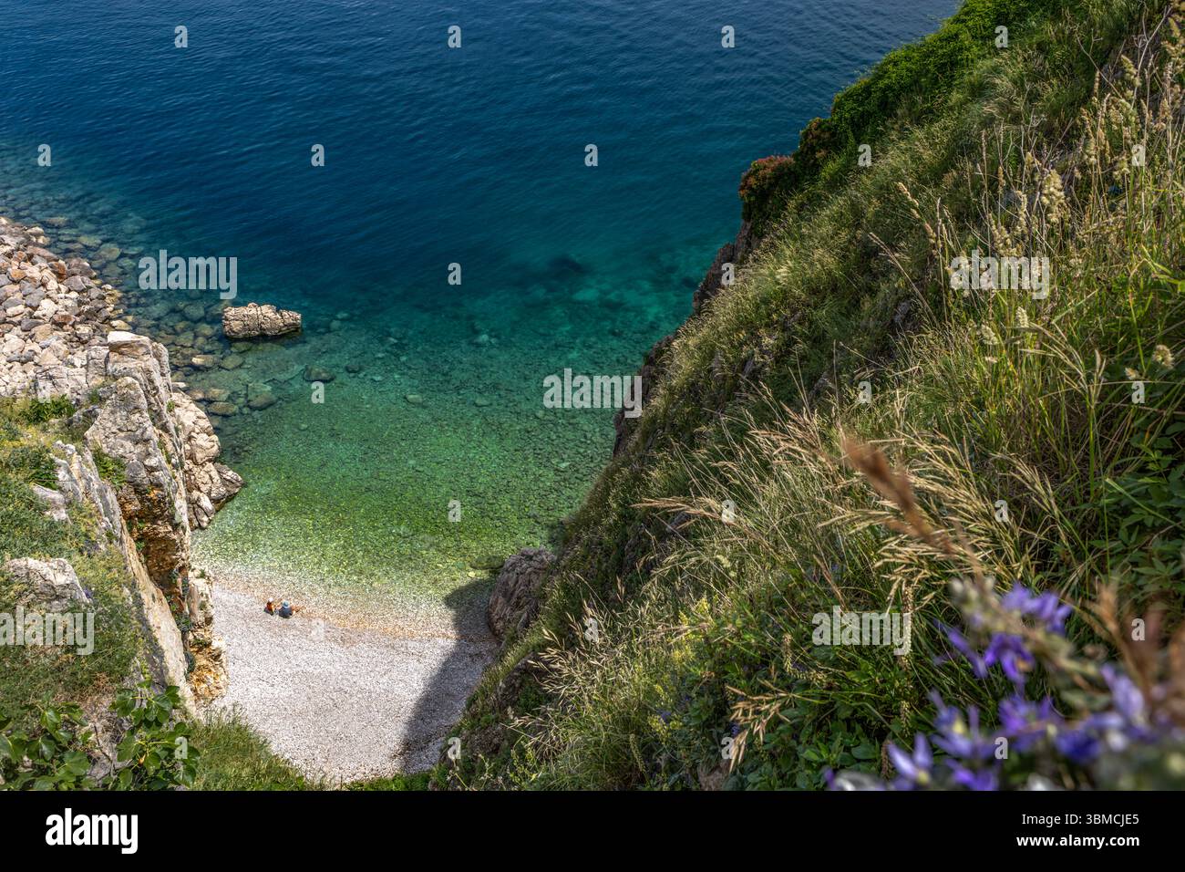 Blick von oben auf das Panorama der Stadt Vrbnik und einen kleinen versteckten Strand zwischen hohen Felsen, eine Touristenattraktion versteckter Kieselstrand auf der Insel KR Stockfoto