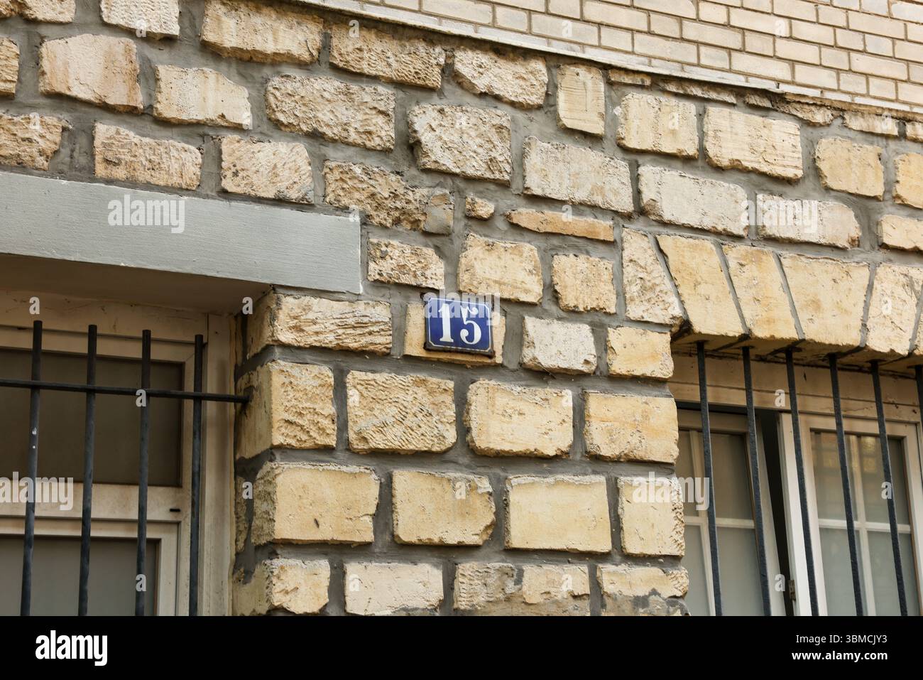 Nahaufnahme eines verwitterten, rustikalen, beigefarbenen Steingebäudes. Eine kleine, dunkelblaue Tafel mit der Zahl 15 ist an der Wand angebracht. Das Bild e Stockfoto