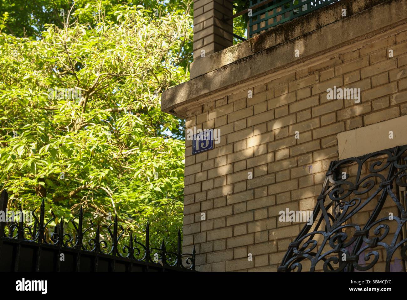 Eine Nahaufnahme des Außenbereichs eines Gebäudes mit einer blauen Nummernplakette „15“ auf einer beigefarbenen Ziegelwand. Die Szene ist in Sonnenlicht getaucht, mit Schatten cas Stockfoto