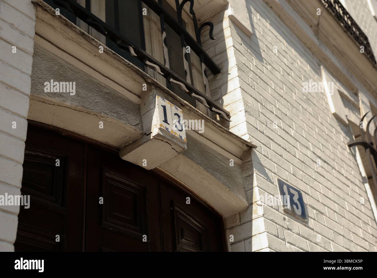 Eine detaillierte Nahaufnahme erfasst die Nummer 13 auf einem verwitterten, weißen Backsteingebäude. Die dunkelbraune Holztür und der verzierte Metallbalkon Stockfoto