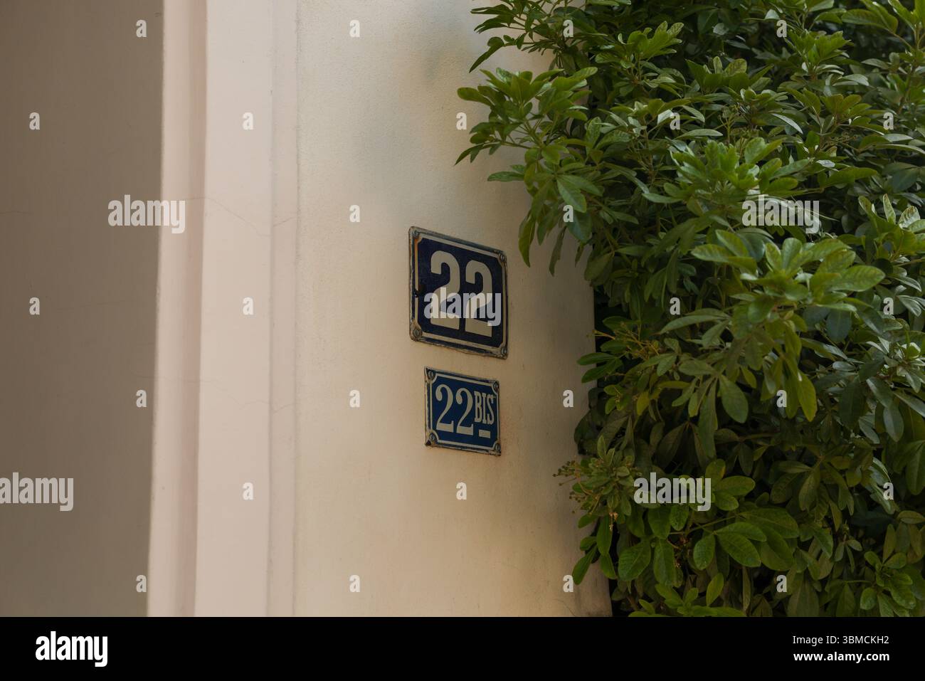 Eine Nahaufnahme von zwei alten Hausnummern 22 und 22 bis, die an einer beigefarbenen Wand befestigt sind. Die Zahlen sind dunkelblau mit weißer Schrift und zeigen Zeichen von Stockfoto