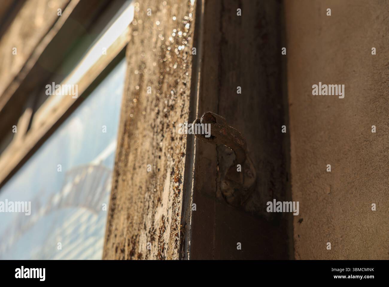 Bei einer detaillierten Nahaufnahme wird ein rostiger Metallriegel auf einem alten, verwitterten Holzrahmen erfasst. Die Textur des Holzes und Metalls ist Promin Stockfoto