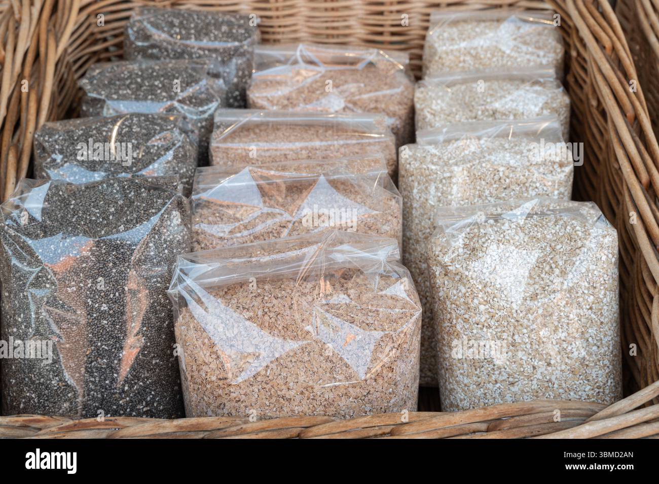 Eine lebendige Sammlung von verschiedenen Getreidearten und Samen, die elegant in einem gewebten Korb auf einem lokalen Markt präsentiert werden Stockfoto