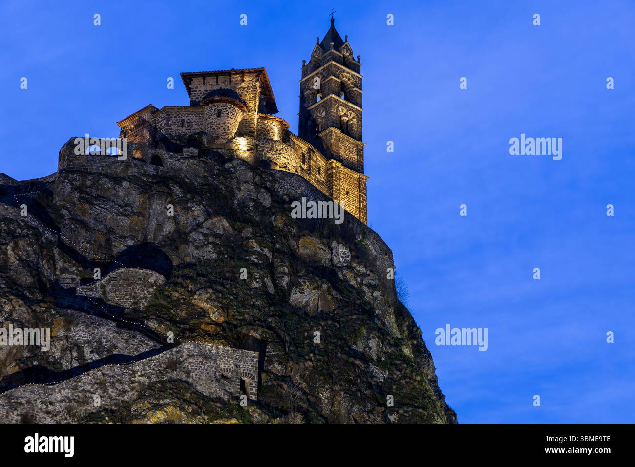 Blick aus einem tiefen Winkel auf die Kapelle Saint-Michel d'Aiguilhe in der Abenddämmerung auf einem vulkanischen Gipfel vor dem tiefblauen Abendhimmel in Aiguilhe, Frankreich. Stockfoto