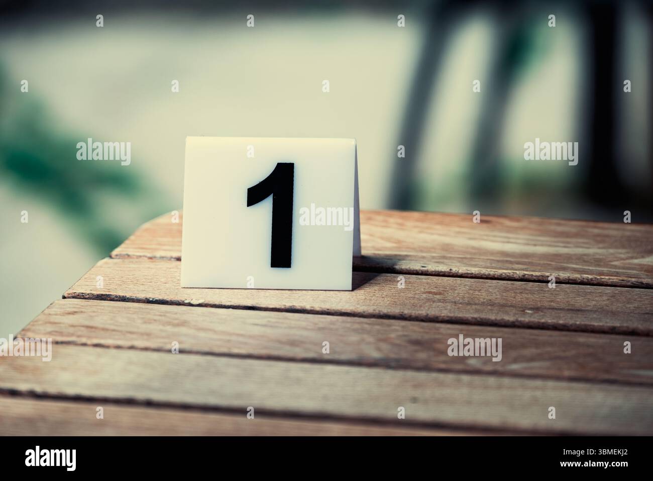 Eine weiße Kachel mit der Zahl 1 steht auf einem Holztisch, der wahrscheinlich als Tischnummer für die Gäste dient. Stockfoto