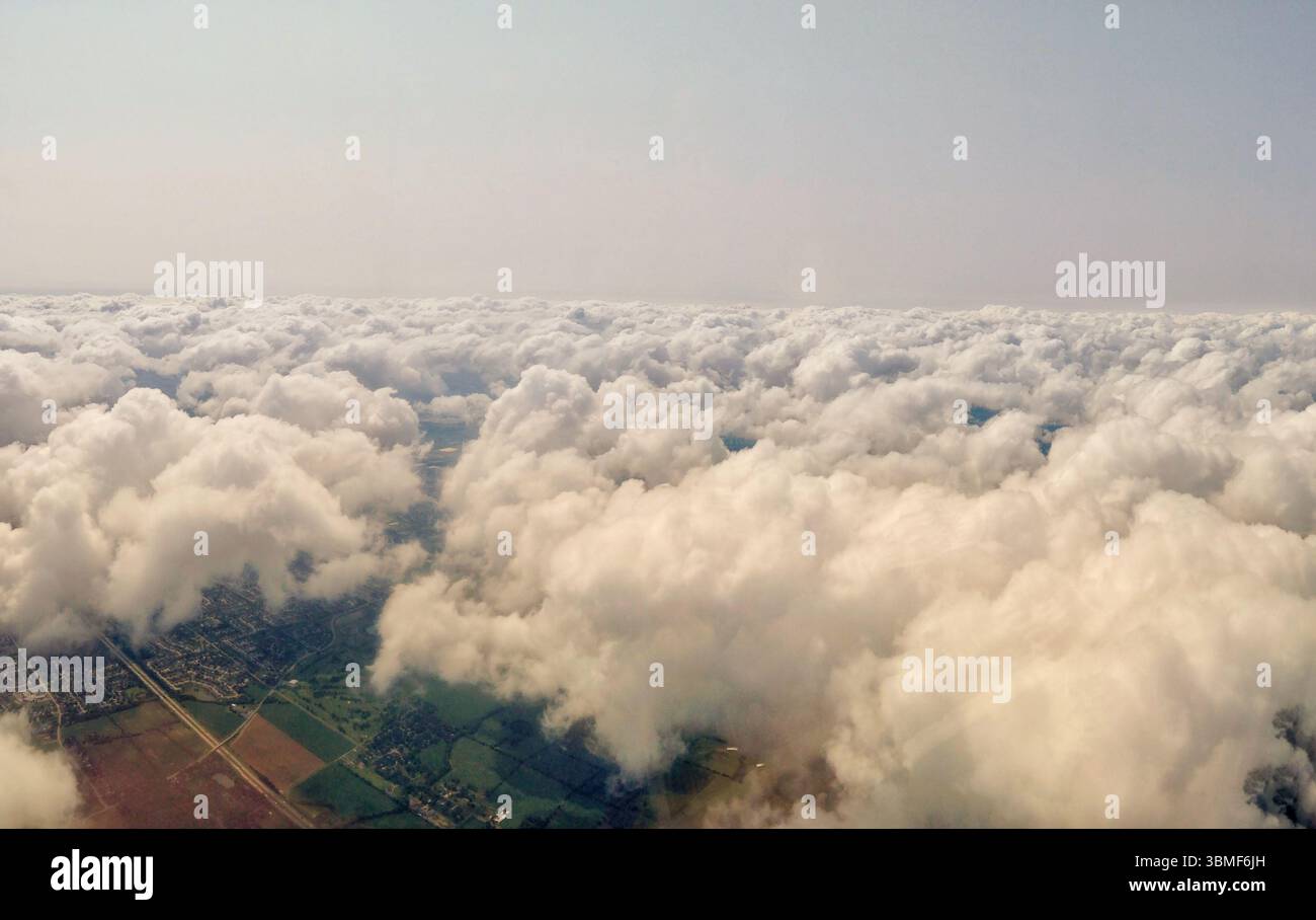 Ein fesselndes Luftpanorama mit flauschigen Wolken, die eine Mischung aus städtischen und ländlichen Gebieten darunter bedecken. Stockfoto
