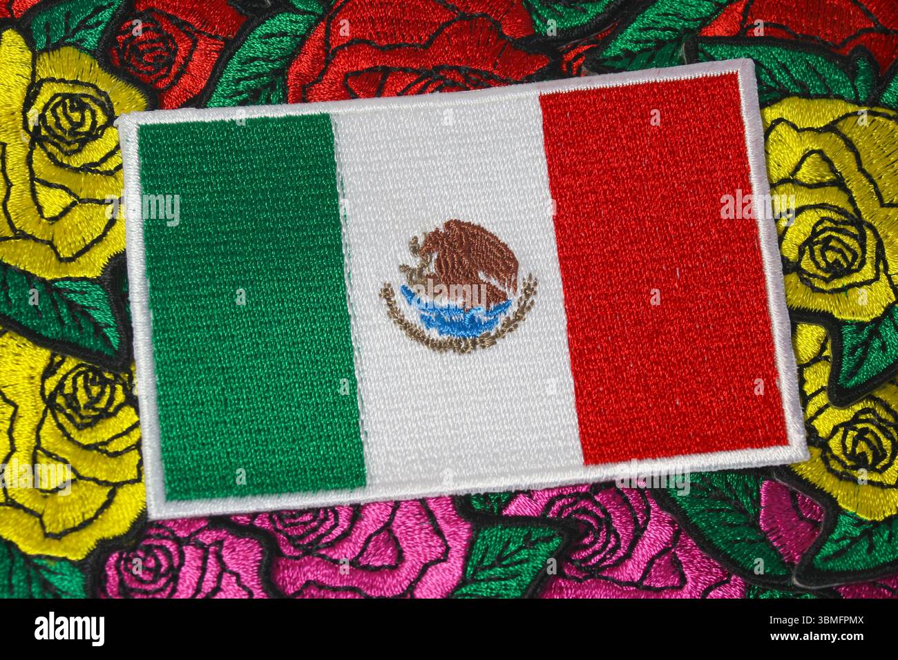 Umweltfreundliche, gestickte mexikanische Flagge auf farbenfrohen, handgefertigten Rosentextilien symbolisiert Kultur und nachhaltiges Handwerk. Stockfoto