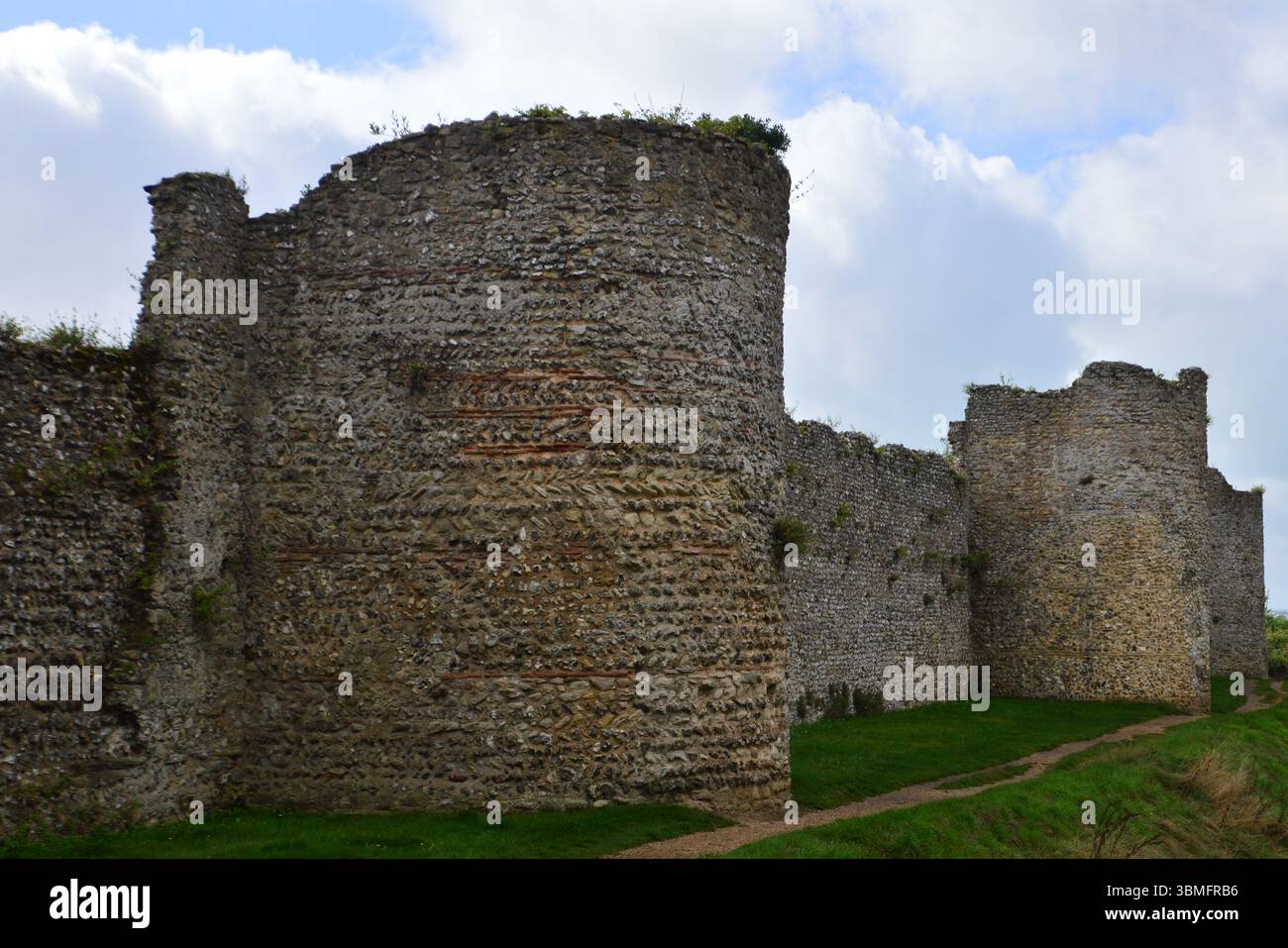 Blick auf die Mauern von Portchester Castle in Hampshire, England, im August erfasst. Mittelalterliche Steinmauern stehen unter einem dramatischen Himmel. Stockfoto