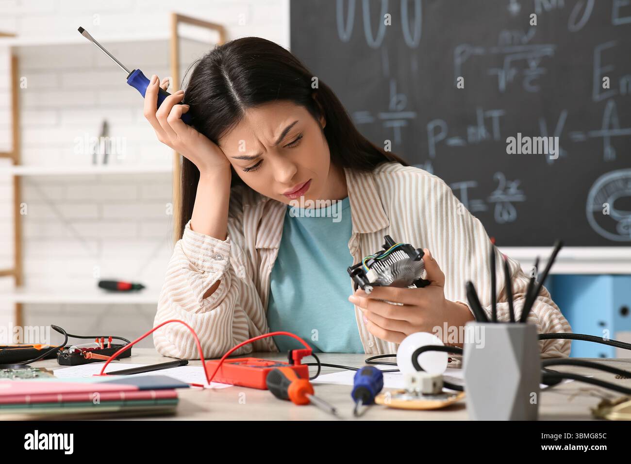 Verärgerte Erfinderin mit Schraubendreher und Computerlüfter am Tisch in der Werkstatt Stockfoto