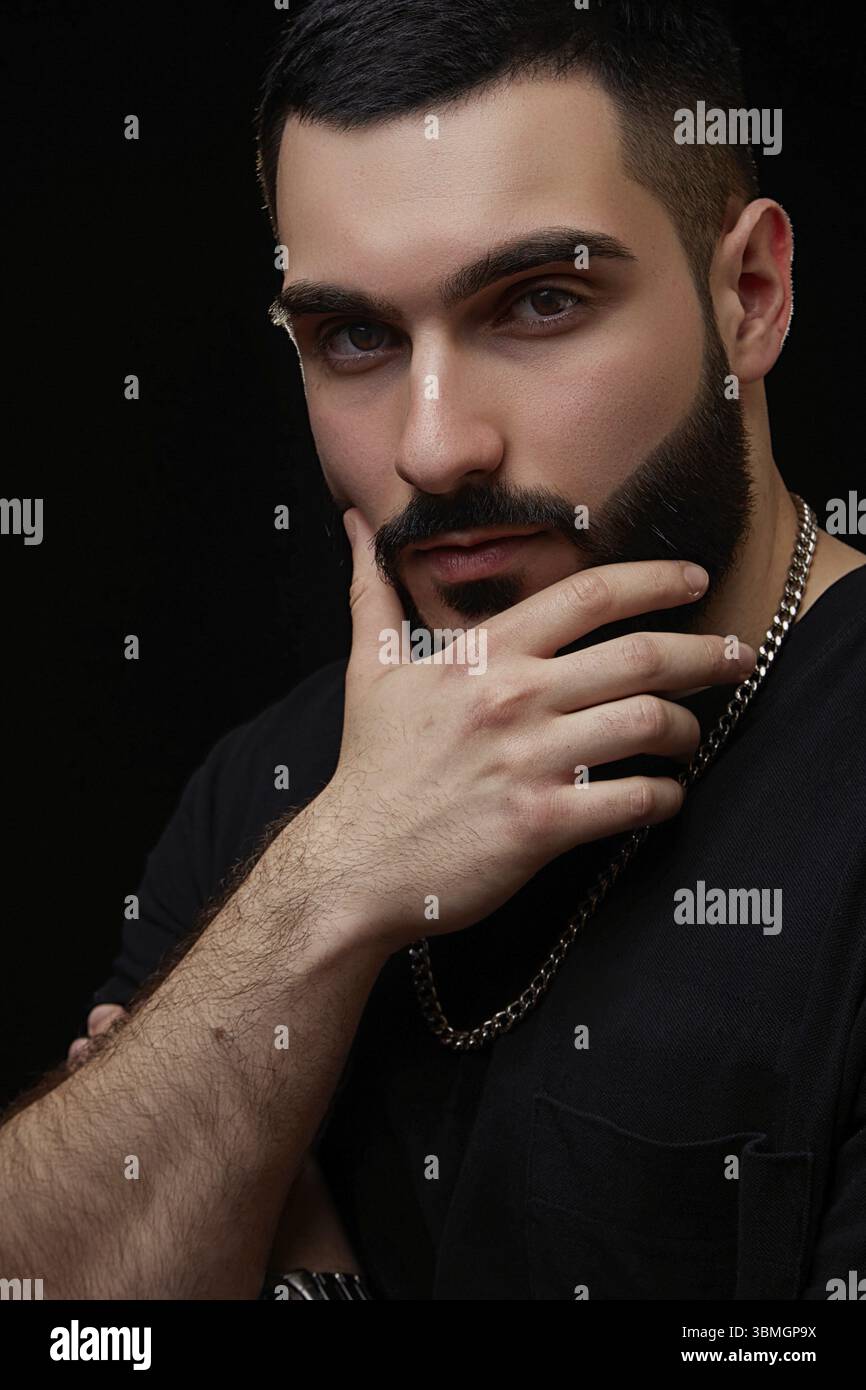 Ein dramatisches Porträt eines jungen seriösen Mannes, Musikers, Sängers, Rappers mit einem Bart in schwarzer Kleidung auf einem schwarzen isolierten Hintergrund. Er denkt an Sorgfalt Stockfoto