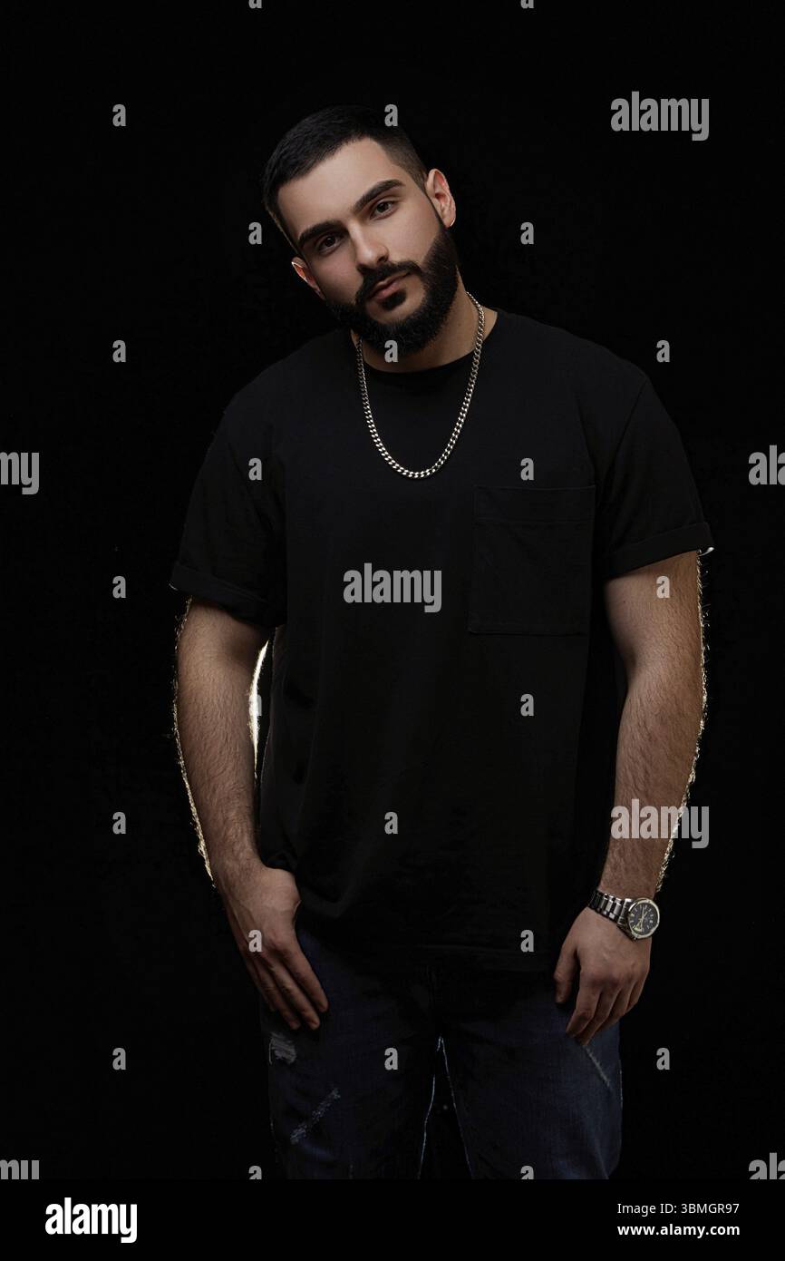 Nahaufnahme eines dramatischen Porträts eines jungen ernsthaften Mannes, Musikers, Sängers, Rappers mit einem Bart in schwarzer Kleidung auf einem schwarzen isolierten Hintergrund Stockfoto