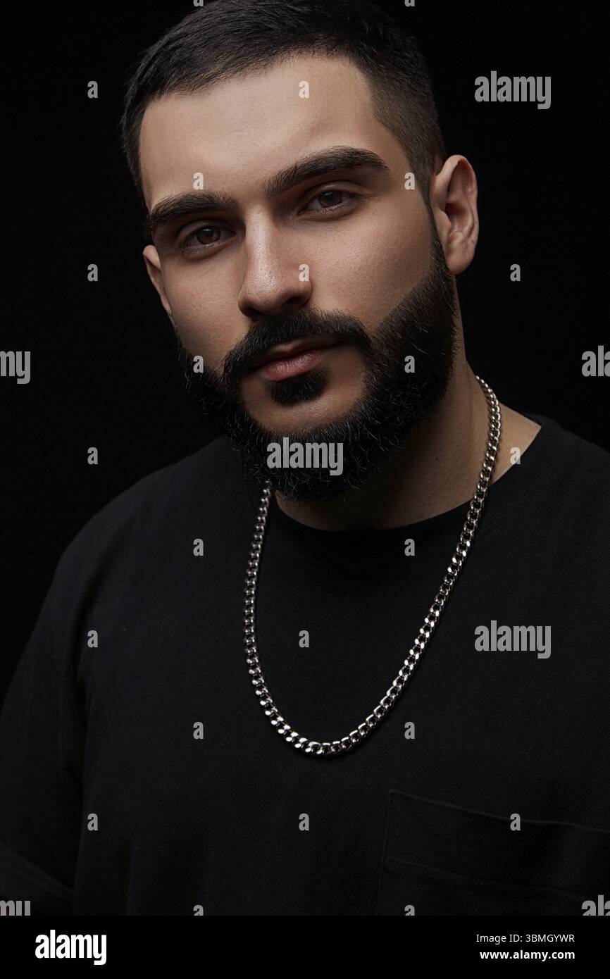 Nahaufnahme eines dramatischen Porträts eines jungen ernsthaften Mannes, Musikers, Sängers, Rappers mit einem Bart in schwarzer Kleidung auf einem schwarzen isolierten Hintergrund Stockfoto