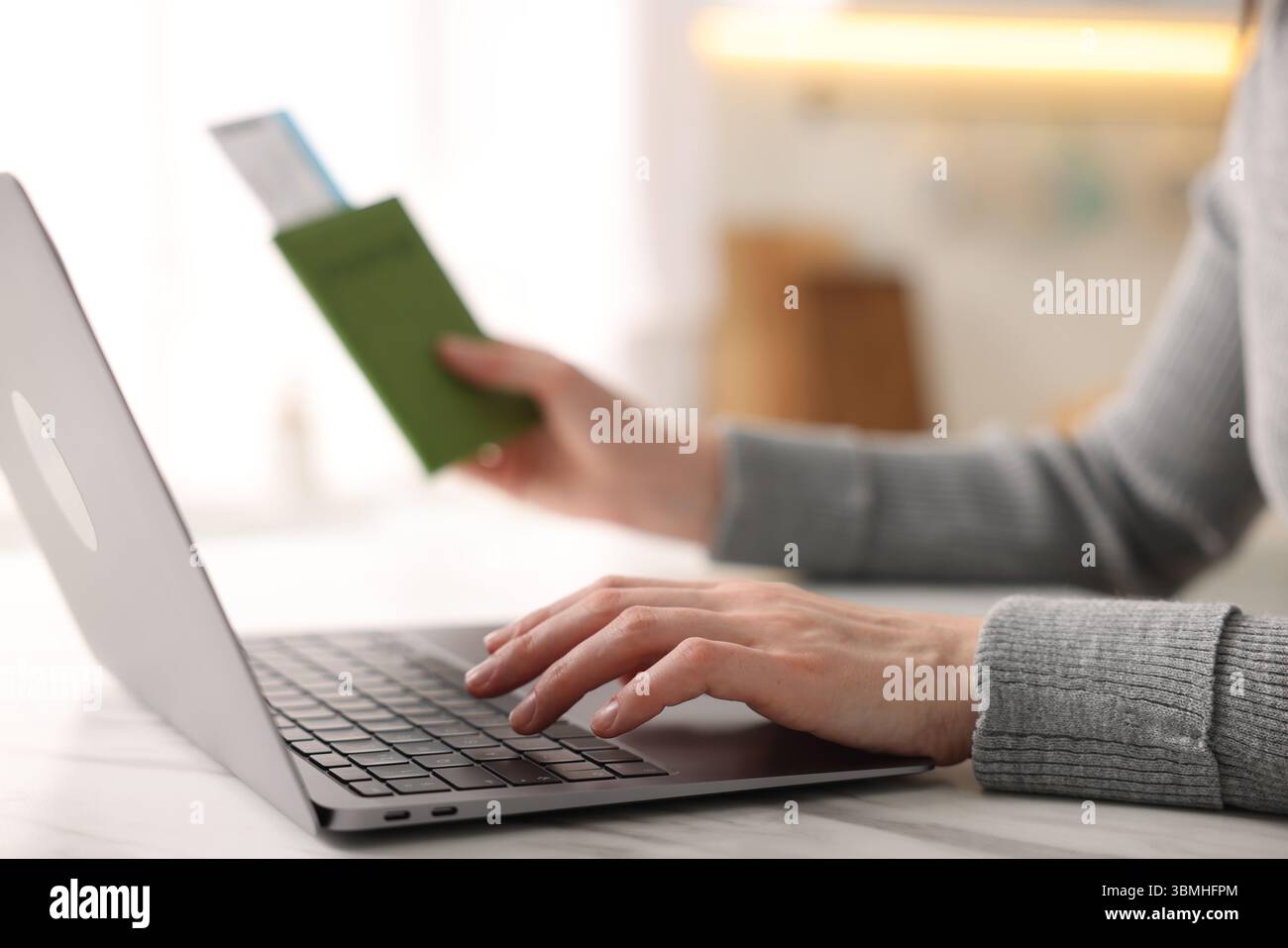 Frau mit Reisepass und Flugticket mit Laptop an weißem Marmortisch drinnen, Nahaufnahme Stockfoto