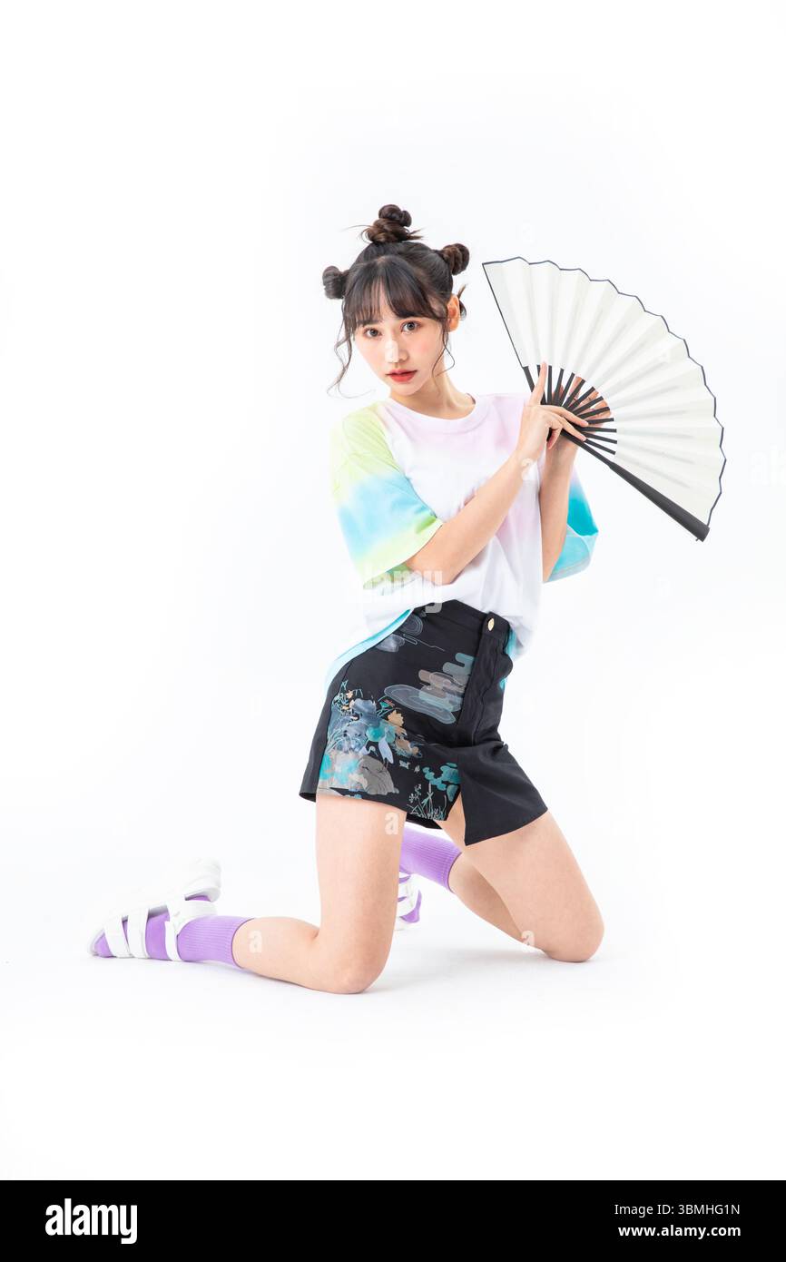 Eine schöne junge Studentin in einem kurzen Rock im chinesischen Stil hält ein traditionelles chinesisches Papier fan Stockfoto