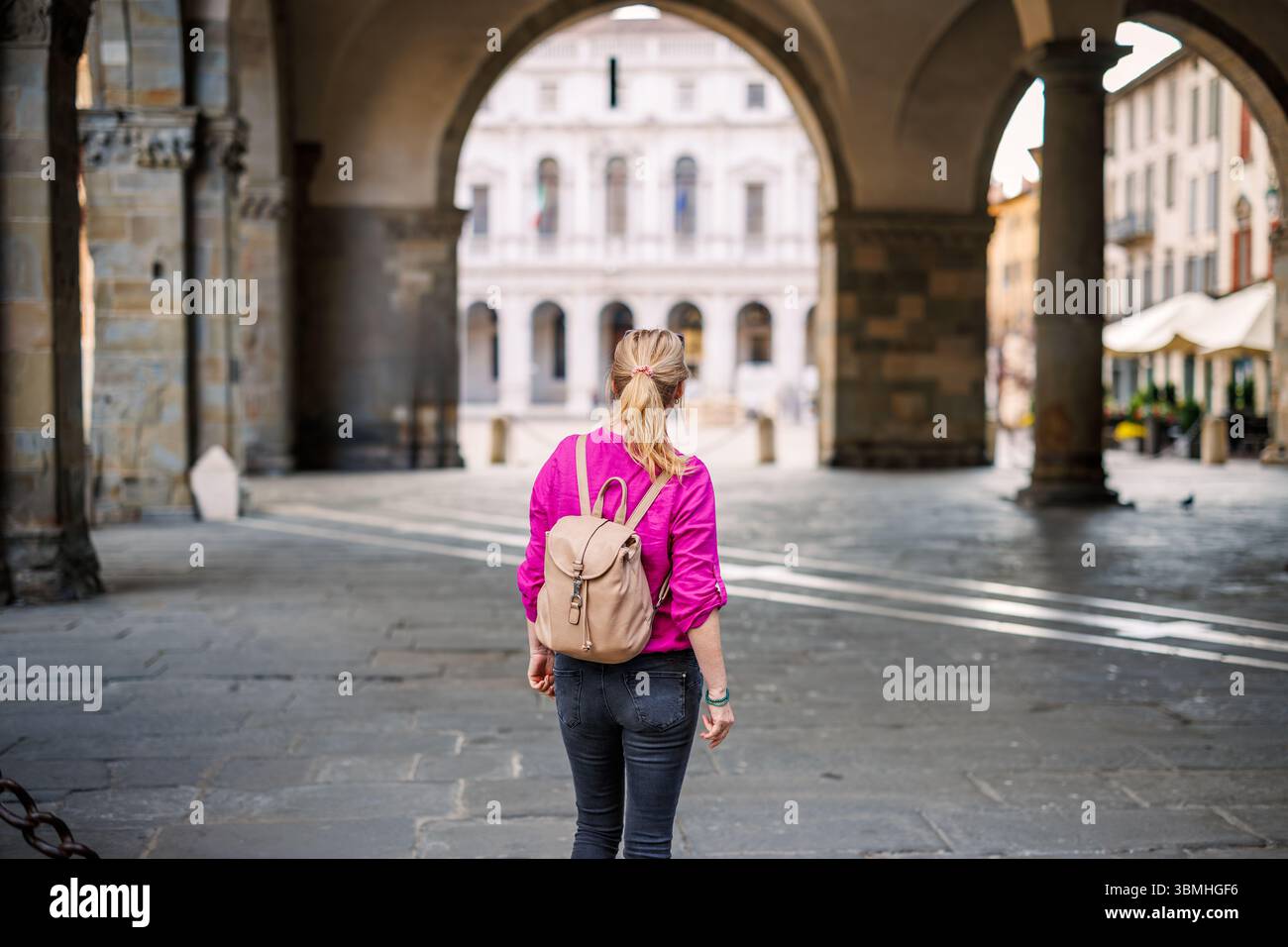 Frau, die unter Bogenarchitektur auf der Piazza Duomo steht und das Reiseziel Bergamo, Italien, genießt. Solo-weibliche Touristen, die die europäische Stadt erkunden Stockfoto