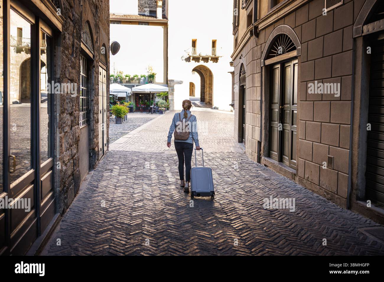 Frau, die mit Koffer durch die alte Steinstraße in Bergamo, Italien, im Sommer alleine reist Stockfoto