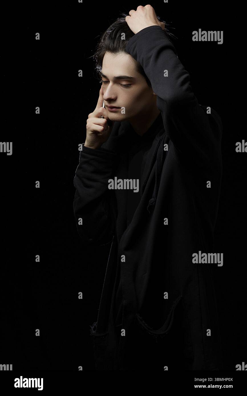 Junger kerl in einem schwarzen Hoodie auf einem schwarzen hintergrund mit einem handlich in seinen haenden Stockfoto