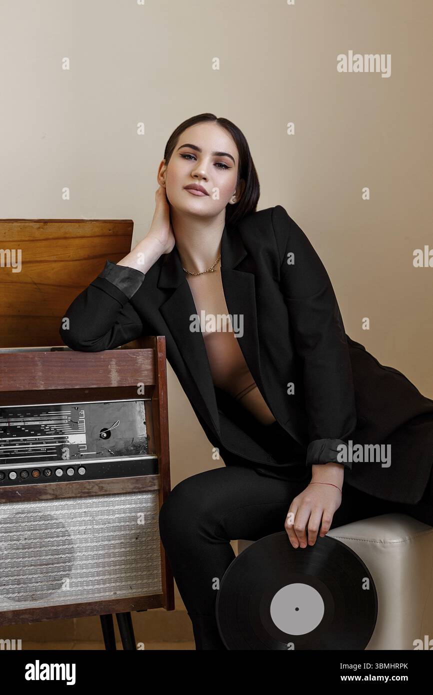 Eine schoene kaukasische junge Frau in einer schwarzen Hosentasche und schwarzen Sandalen posiert neben einem Vintage-Blockflöte mit einem Grammophon-re Stockfoto