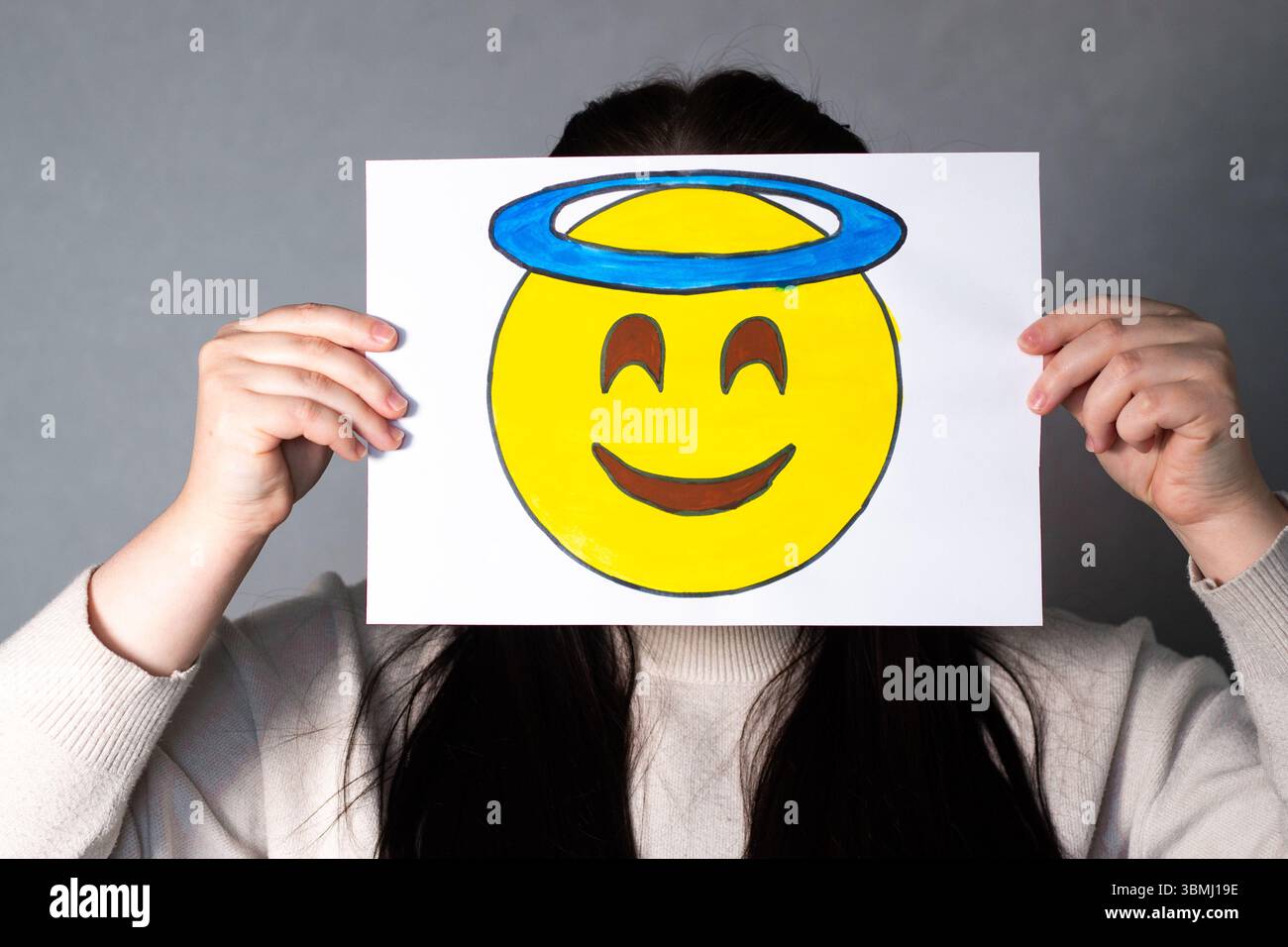 Frau mit lächelndem Winkel-Emoji-Maske vor dem Gesicht. Social Media Trends, Gen Z Marketing, World Emoji Day 17. Juli. Stockfoto