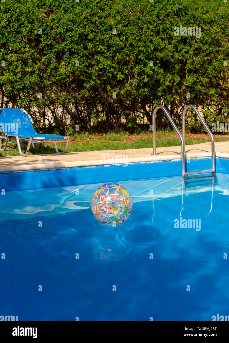 Sommerszene mit einem aufblasbaren Ball, der im Swimmingpool und in der Nähe einer Sonnenliege schwimmt. Helle, entspannende Atmosphäre, perfekt für Urlaub, Freizeit, TRA Stockfoto