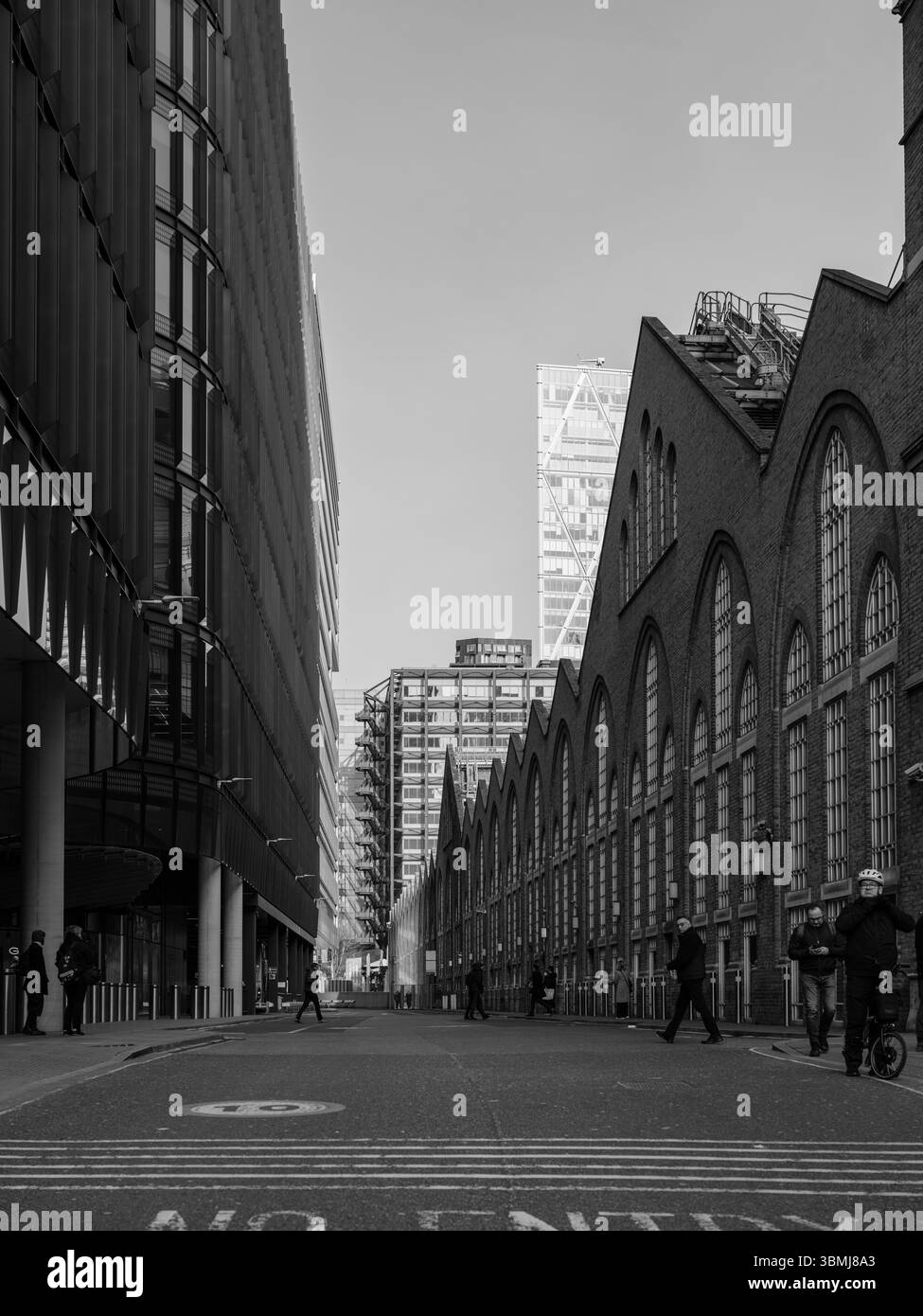 Vereinigtes Königreich, London, 4. Juli 2025. Schwarz-weiß-Blick auf Fußgänger, die entlang einer Straße in London laufen, umgeben von modernen und industriellen Bu Stockfoto