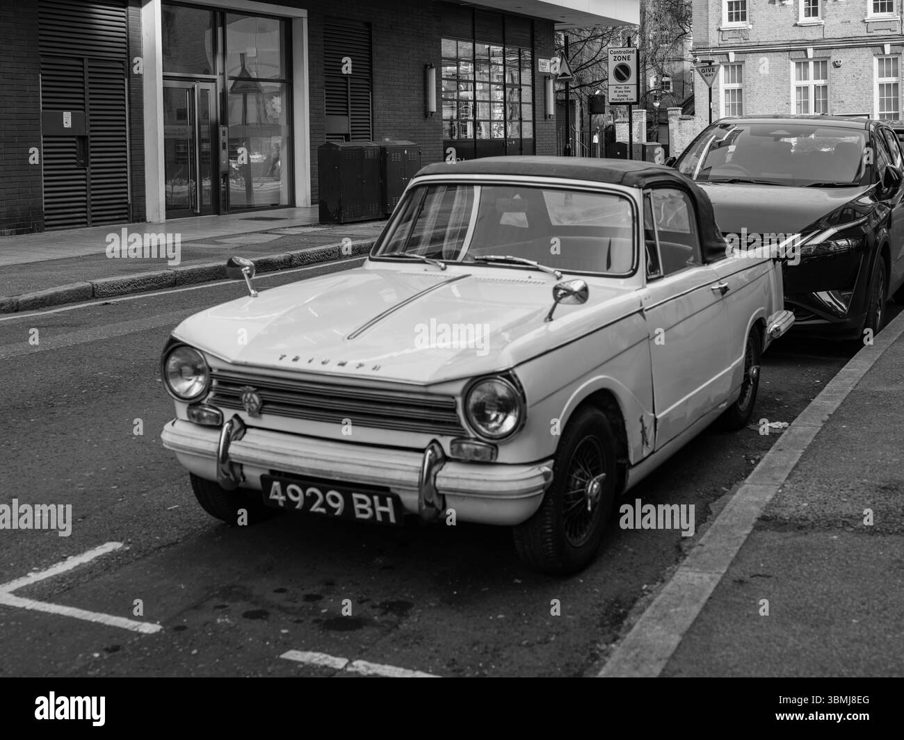 Vereinigtes Königreich, London, 4. Juli 2025. Schwarz-weiß-Bild eines klassischen Triumph Herald Cabriolets, das auf einer Londoner Straße geparkt ist und britische M reflektiert Stockfoto