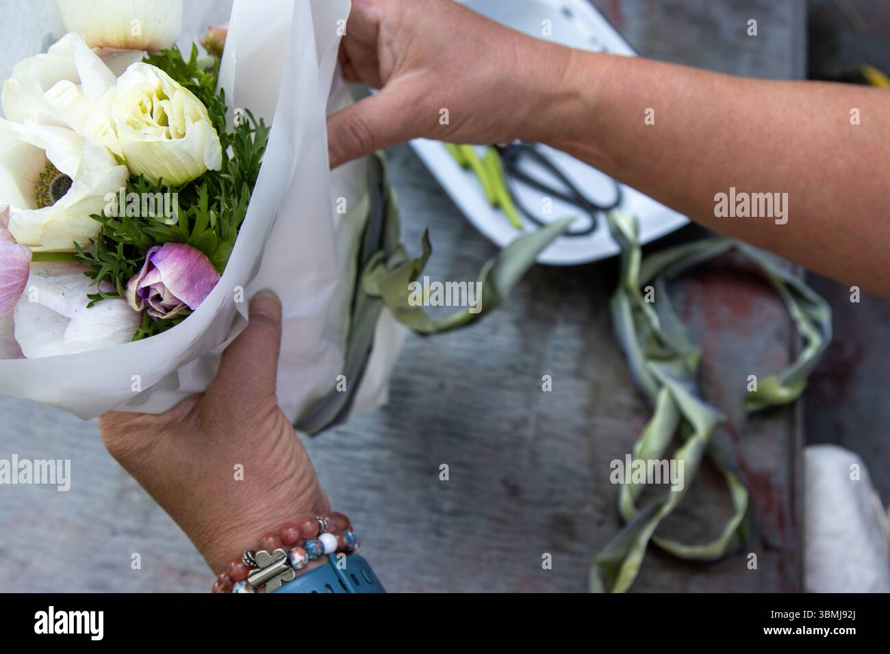 Hände wickeln Papierstrauß von Anemonen mit salbeigrünem Band Stockfoto