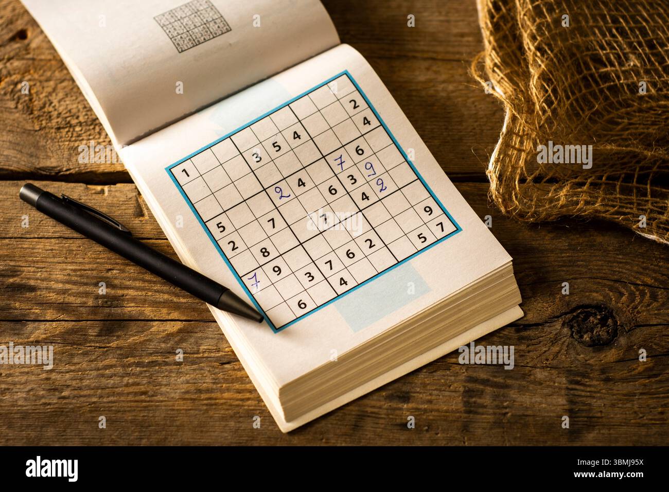 Ein offenes Sudoku-Puzzle-Buch mit einem schwarzen Stift auf den Seiten, vor einem warmen, rustikalen Holzhintergrund, der an Konzentration und Freizeit erinnert. Stockfoto