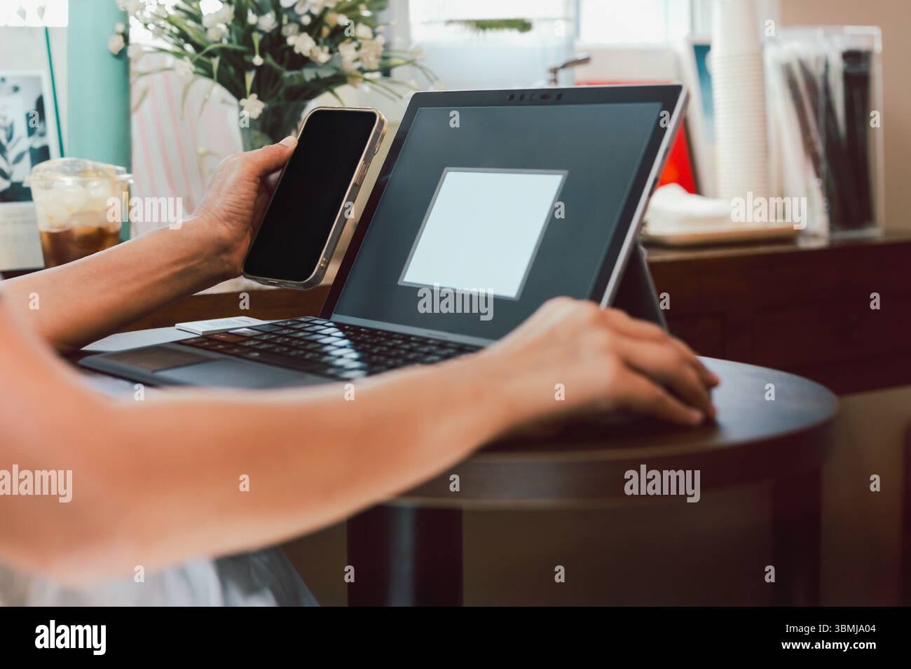 Geschäftsfrau benutzt Handy, während sie am Laptop arbeitet. Stockfoto