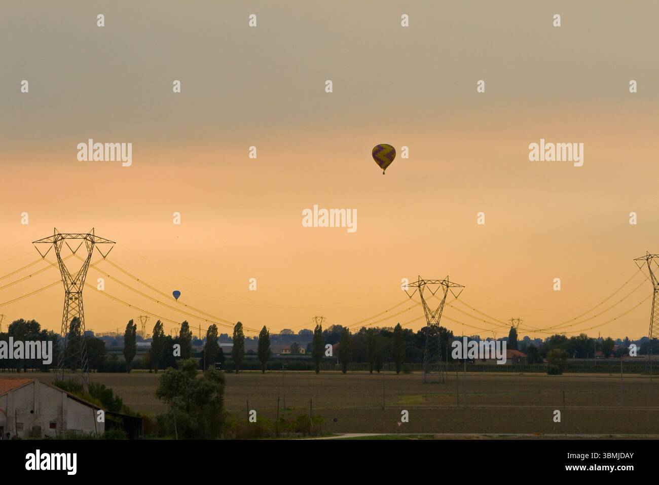 Heißluftballons gleiten bei einem ruhigen Sonnenuntergang über Felder Stockfoto