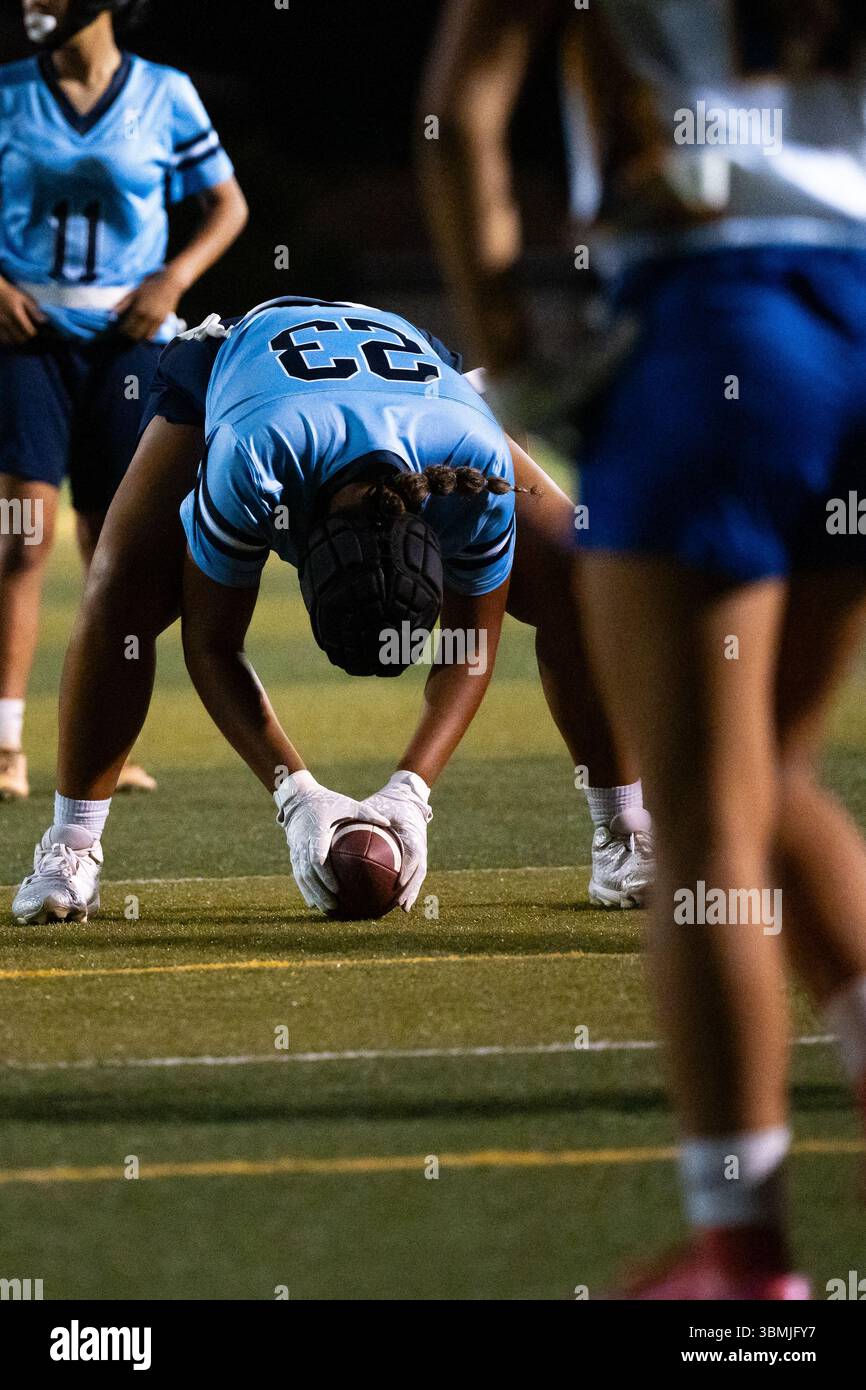 Girls Flag Football Center bereitet sich darauf vor, den Ball beim Nachtspiel zu knacken, in Position mit Fokus und Absicht, Jugendsportler in Aktion unter Licht Stockfoto