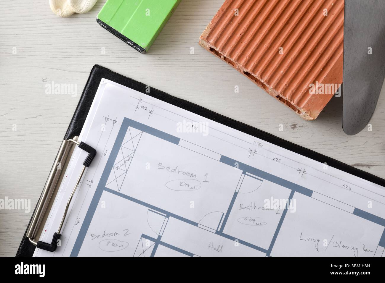 Details mit Mappe mit Bau- oder Renovierungsplänen und umliegenden Elementen wie Ziegeln, Kelle und Meter. Draufsicht. Stockfoto